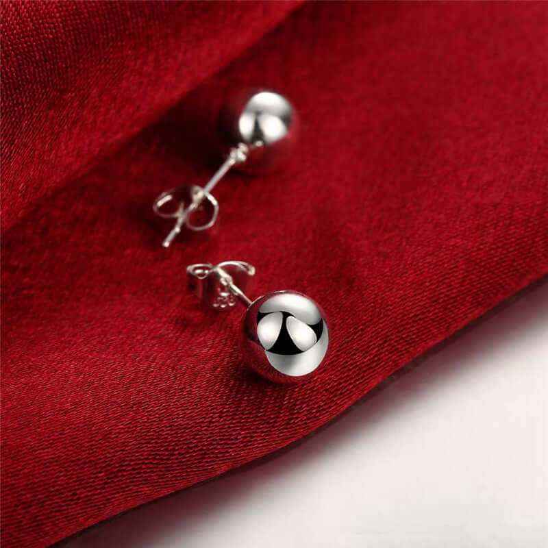 Creative 6M 8M 10M Bead Stud Earrings in silver plating on red fabric.