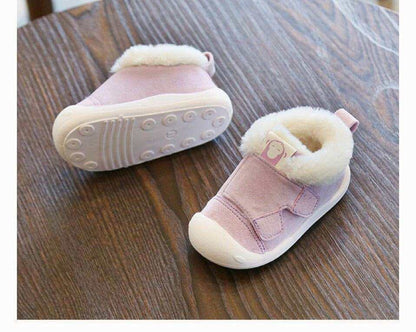 Pink toddler shoes with velvet material and white fluffy lining on a wooden surface.