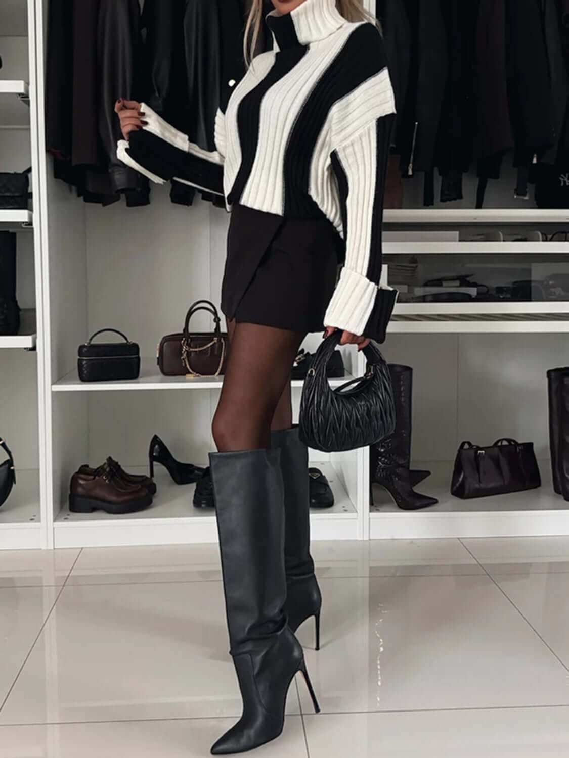 Striped turtleneck dropped shoulder sweater in black and white worn with knee-high boots.