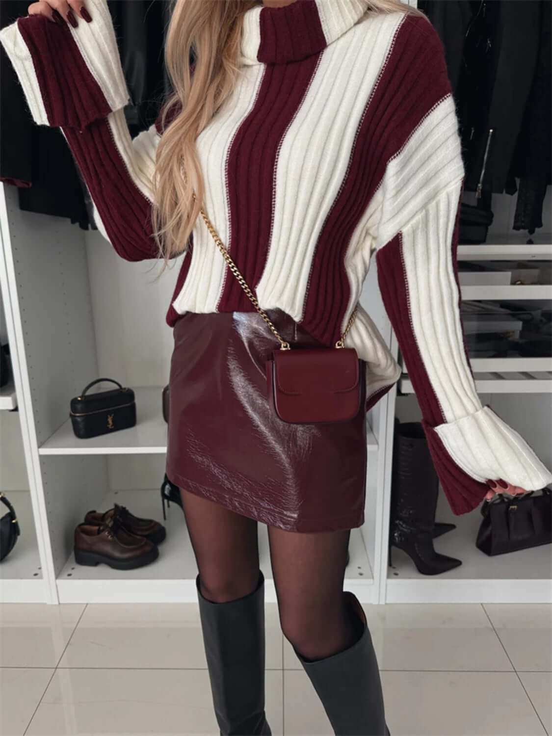 Striped turtleneck dropped shoulder sweater with red and white pattern, paired with a leather skirt and knee-high boots.