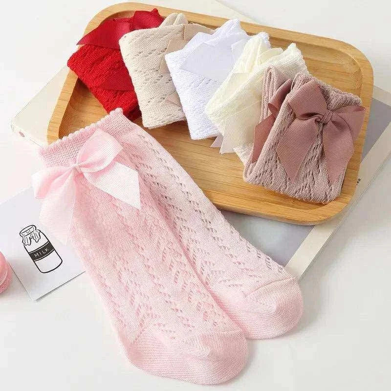 Baby Girls Long Bow Sock with lace detailing in various colors on a wooden tray.