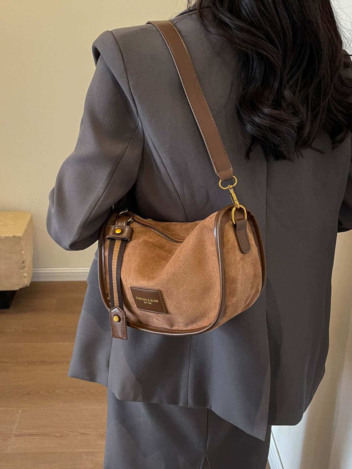 Suede adjustable strap women's shoulder bag in brown, worn with a grey suit.