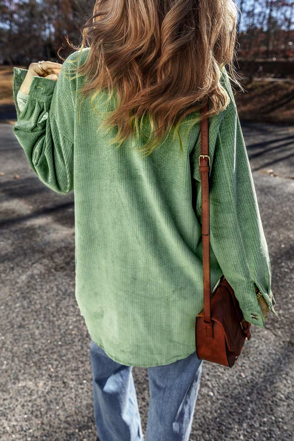 Pocketed collared neck button up shacket in green worn with jeans outdoors.